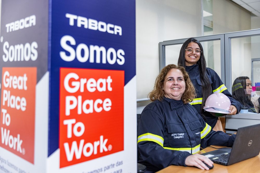 Duas profissionais da Taboca, uniformizadas, sorriem ao lado de um totem Somos Great Place To Work na unidade de Pirapora do Bom Jesus